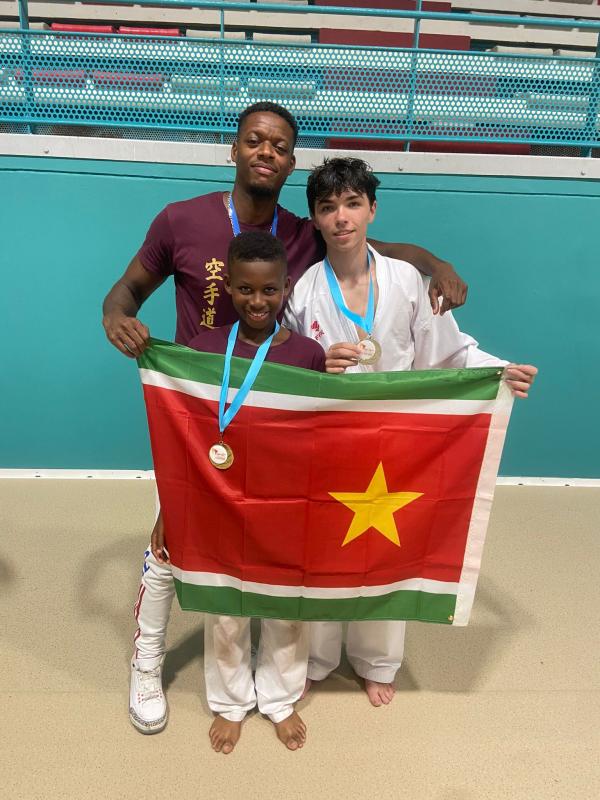 Trois karatékas sur un podium, médailles au cou, tenant un drapeau