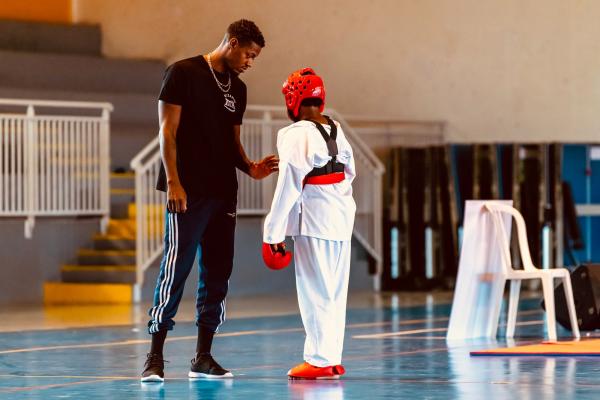 Un encadrant ajuste la protection de tête d’un jeune compétiteur sur le tatami