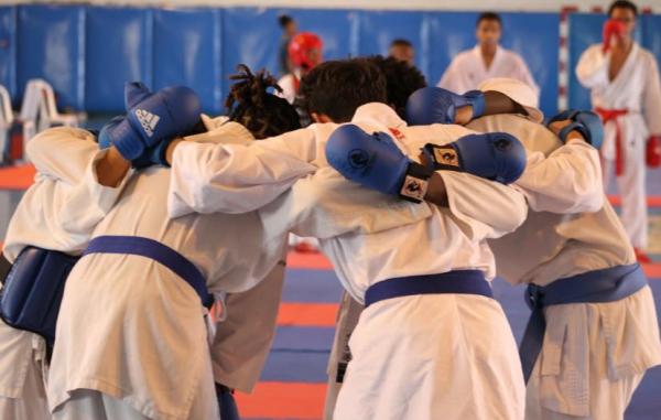 Des karatékas en kimono forment un cercle sur le tatami, bras sur les épaules, vus de dos